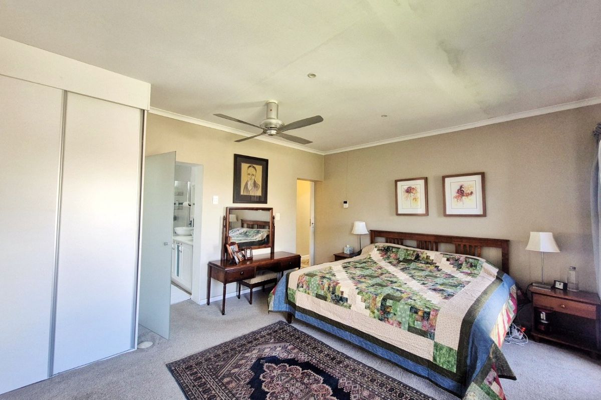 Spacious bedroom featuring a built-in wardrobe, ceiling fan, and direct access to an en-suite bathroom. Note visible ceiling staining requiring attention.