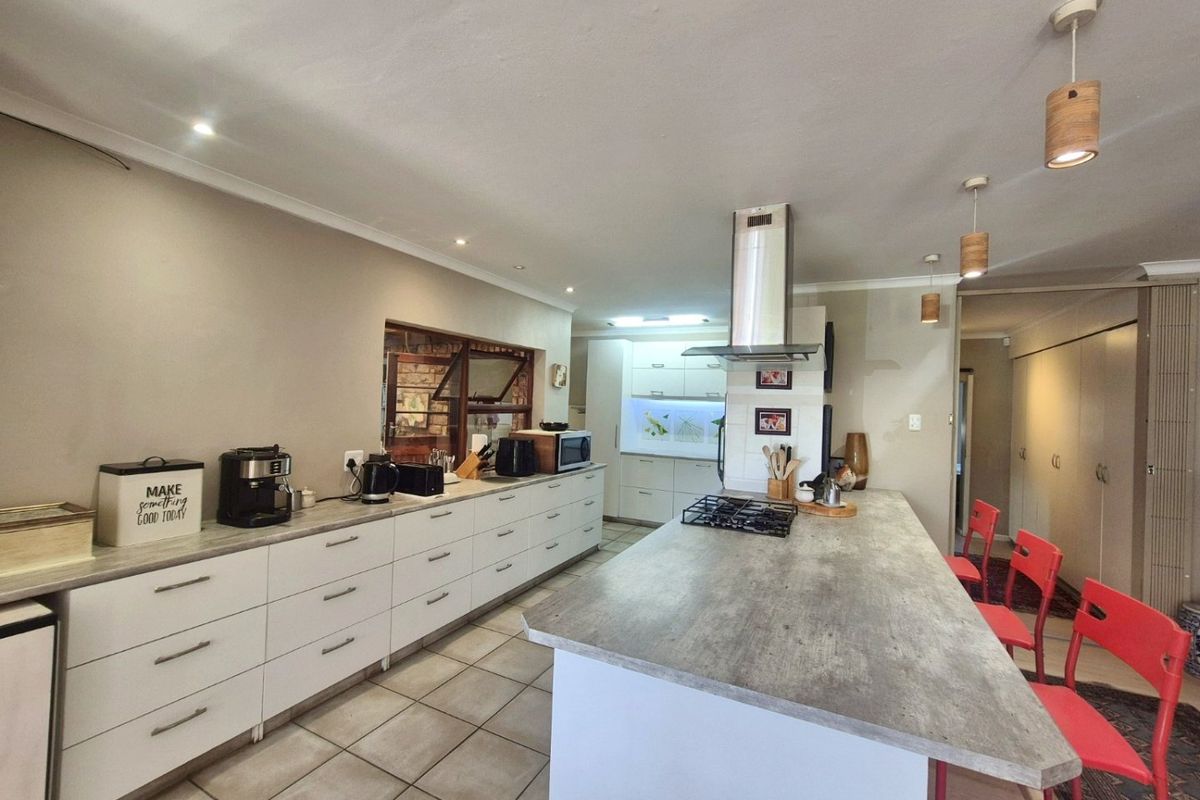 Modern kitchen featuring a large central island with a gas hob, extensive built-in cabinetry, stone-look countertops, and contemporary pendant lighting.