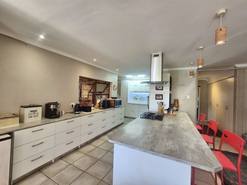 Modern kitchen featuring a large central island with a gas hob, extensive built-in cabinetry, stone-look countertops, and contemporary pendant lighting.