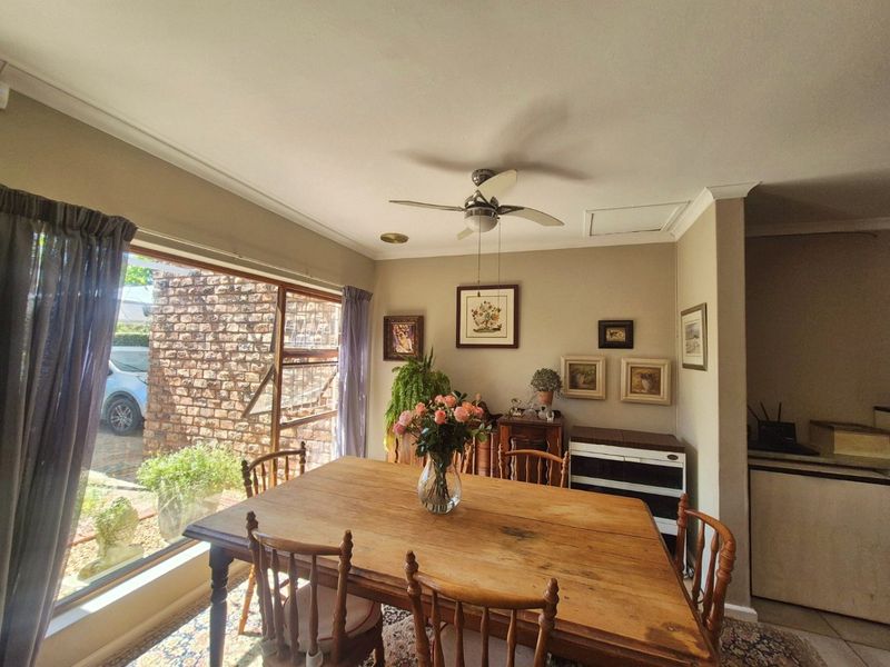 A dining room featuring a ceiling fan, large window with natural light, and tiled flooring, offering a comfortable space for family meals.