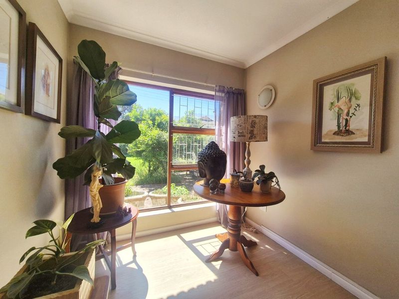 A sunlit living area featuring laminate flooring, coving, and a large window with security bars overlooking the garden.