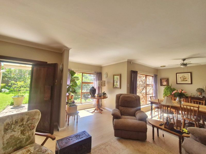 Spacious open-plan living and dining area featuring laminate flooring, coved cornicing, and large windows providing natural light and direct access to the garden.