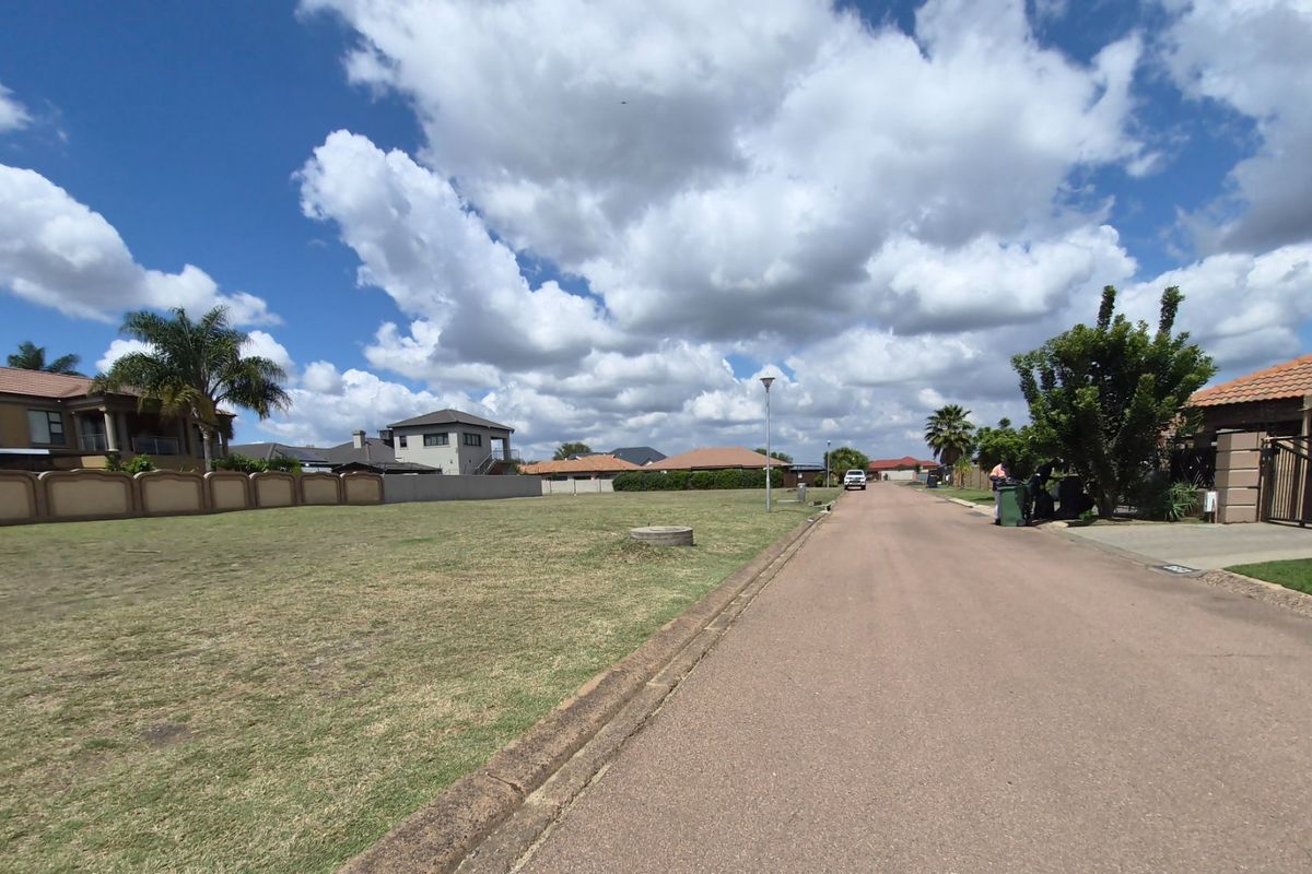 A view of a residential street with a vacant plot of land adjacent to the paved road and curb.