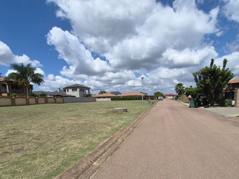 A view of a residential street with a vacant plot of land adjacent to the paved road and curb.