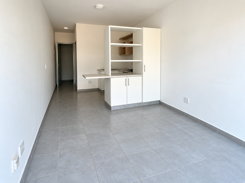 A bright, open-plan living and kitchen area featuring modern tiled flooring, built-in cabinetry, and a functional breakfast counter in a clean, neutral space.