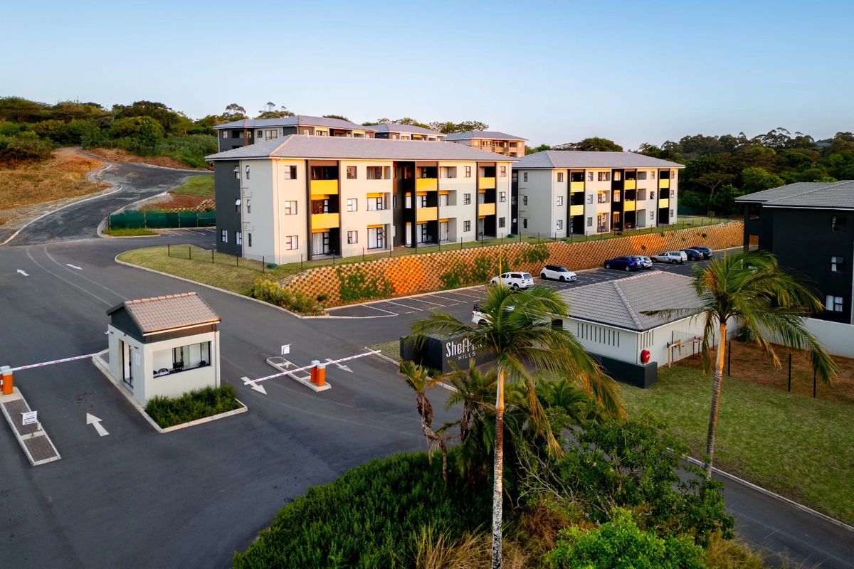 Aerial view of a modern apartment complex featuring a secure gated entrance, paved parking areas, and well-maintained landscaping.