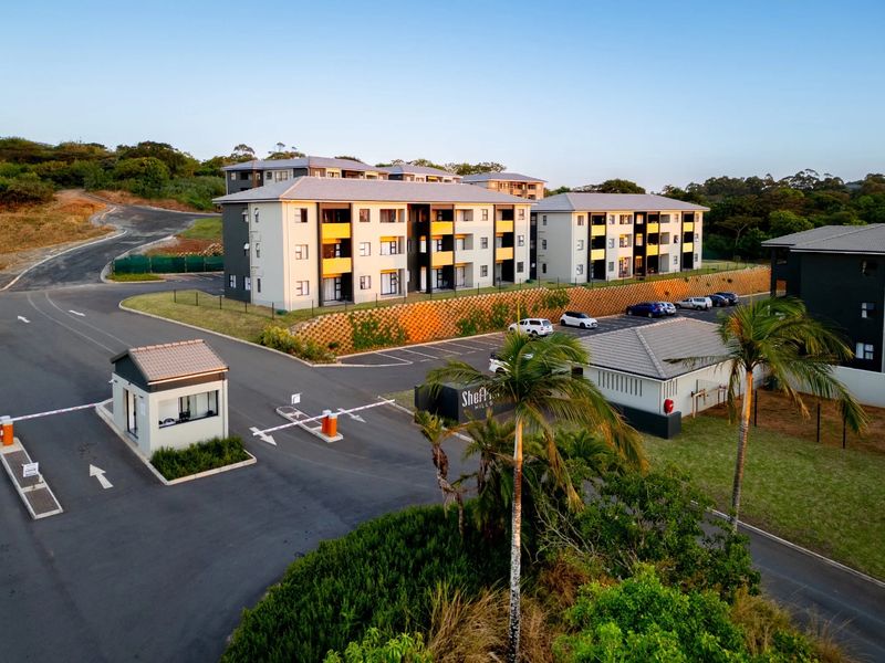 Aerial view of a modern apartment complex featuring a secure gated entrance, paved parking areas, and well-maintained landscaping.