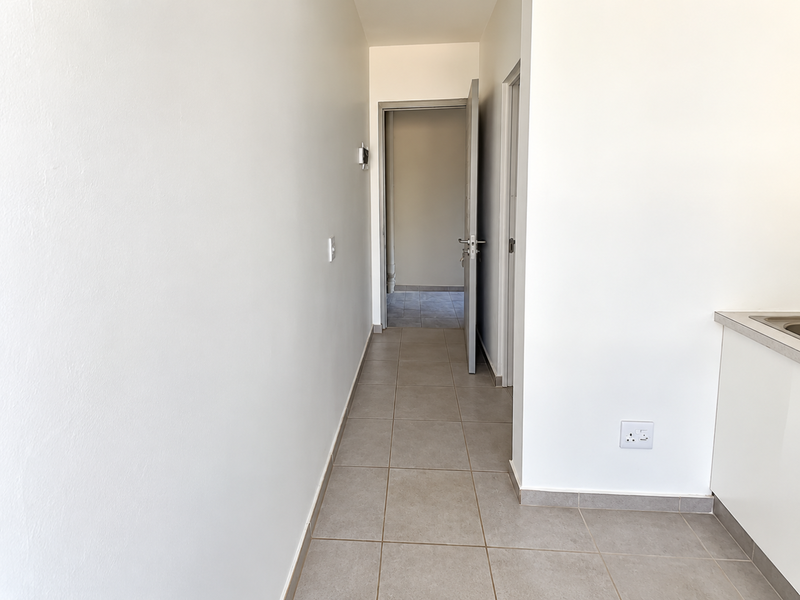 A clean, neutral hallway featuring tiled flooring and access to adjacent rooms, providing a bright and functional transition space within the apartment.