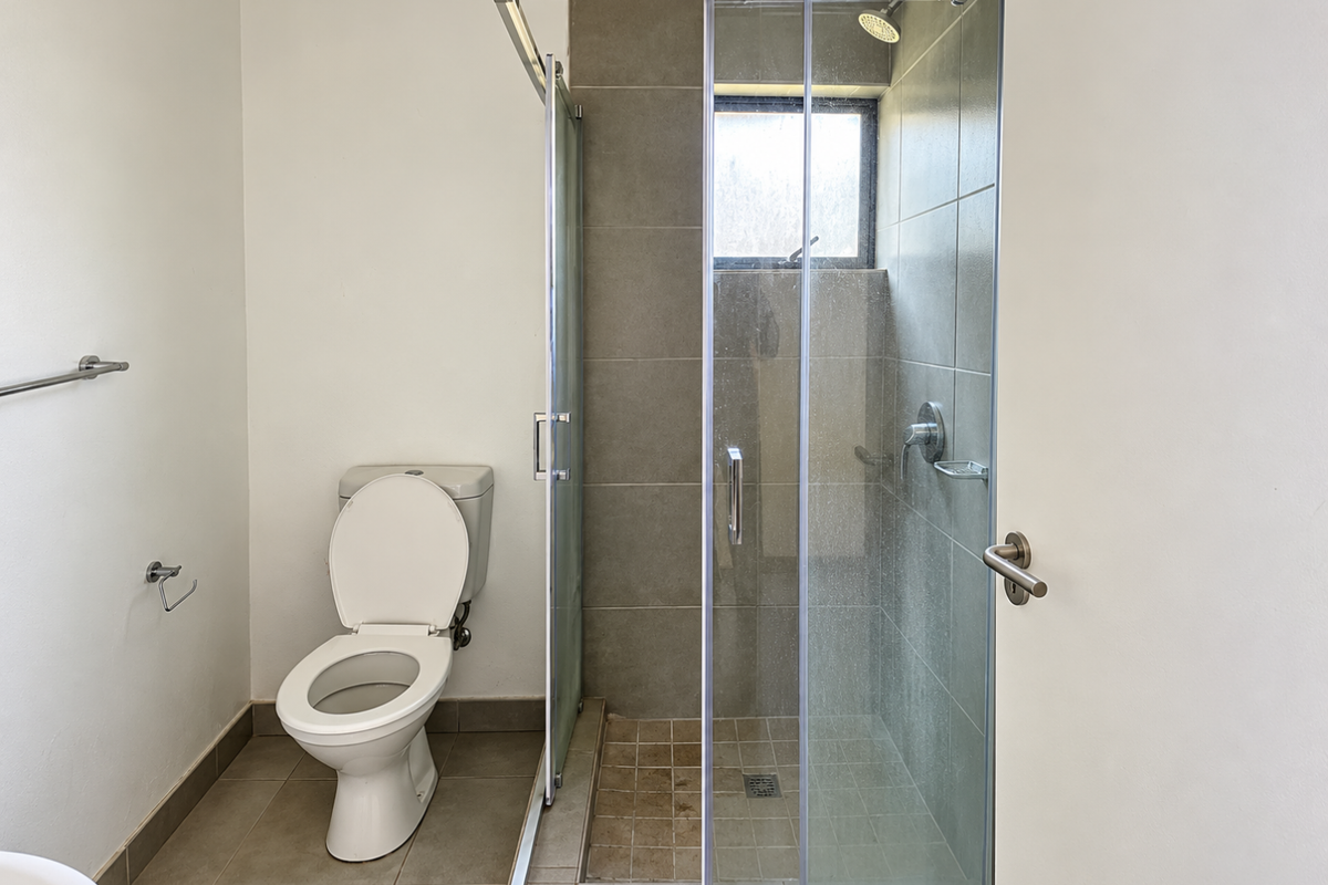 A functional bathroom featuring a glass-enclosed shower with tiled walls and a standard toilet, offering a clean and simple layout.