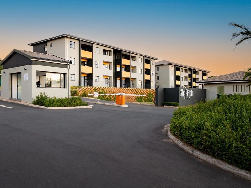 The entrance to Sheffield Hills apartment complex featuring a secure guard house, gated access, and modern multi-story residential buildings.