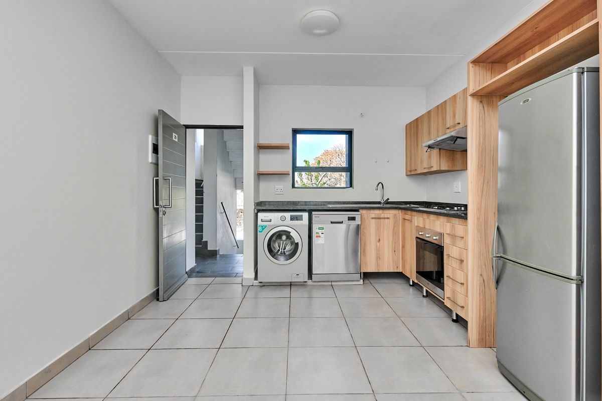 Modern kitchen featuring light wood cabinetry, stone countertops, built-in oven, hob, extractor fan, and tiled flooring with direct access to the entrance.