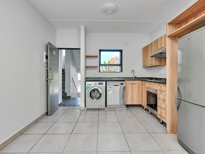 Modern kitchen featuring light wood cabinetry, stone countertops, built-in oven, hob, extractor fan, and tiled flooring with direct access to the entrance.