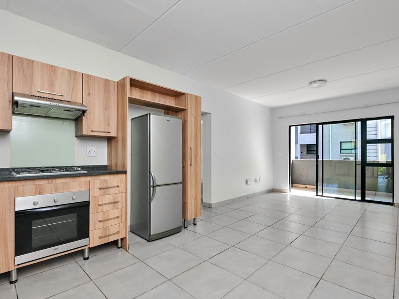 Modern open-plan kitchen and living area featuring light wood cabinetry, granite countertops, tiled floors, and direct access to a private balcony.