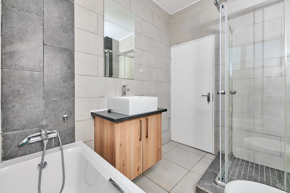 Modern bathroom featuring a vessel sink on a wooden vanity, a separate bathtub, and a glass-enclosed shower with neutral tiled finishes.