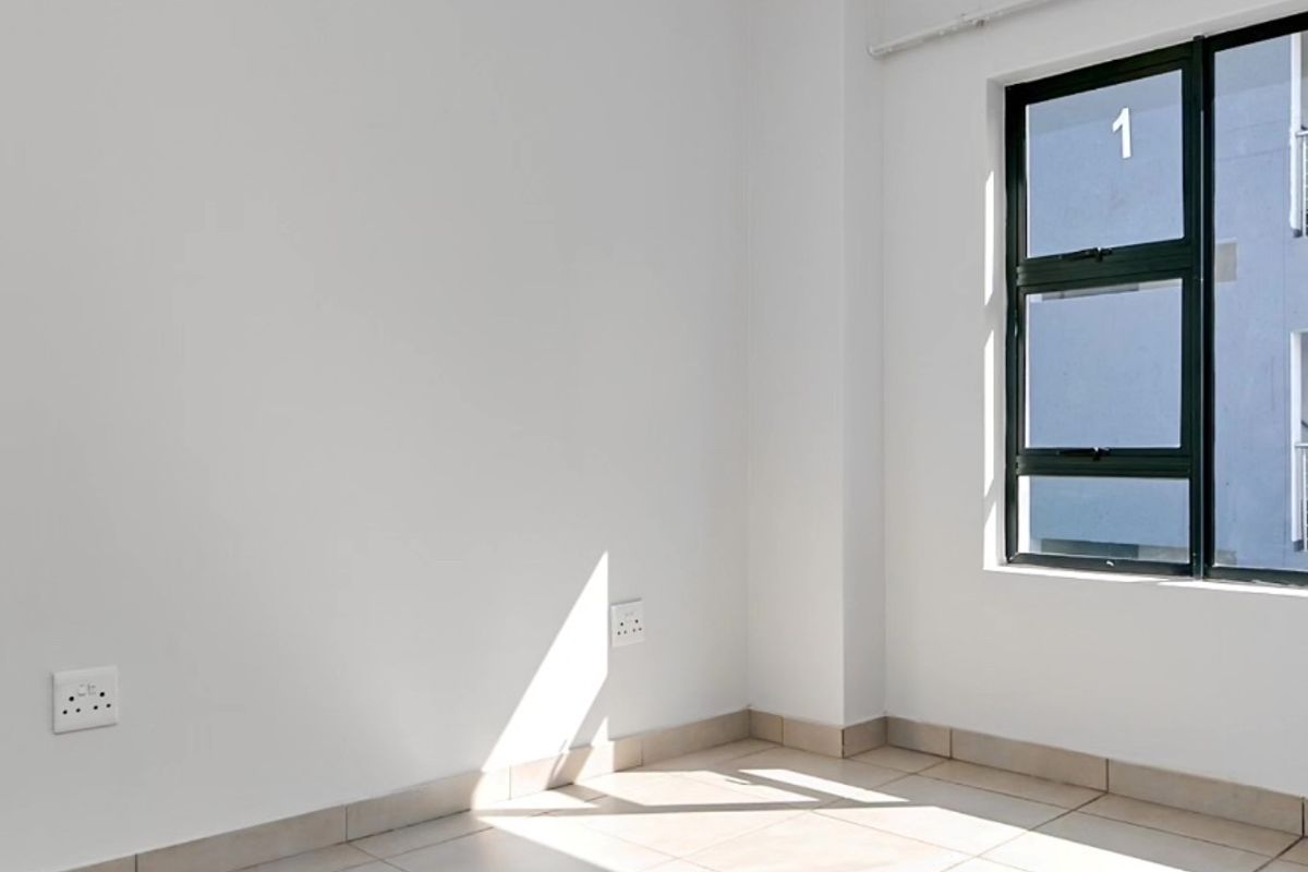 A bright, empty bedroom featuring neutral tiled flooring, clean white walls, and a modern aluminium-framed window.