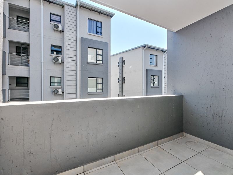 A private apartment balcony featuring tiled flooring and a concrete balustrade, offering an outlook over the complex architecture.