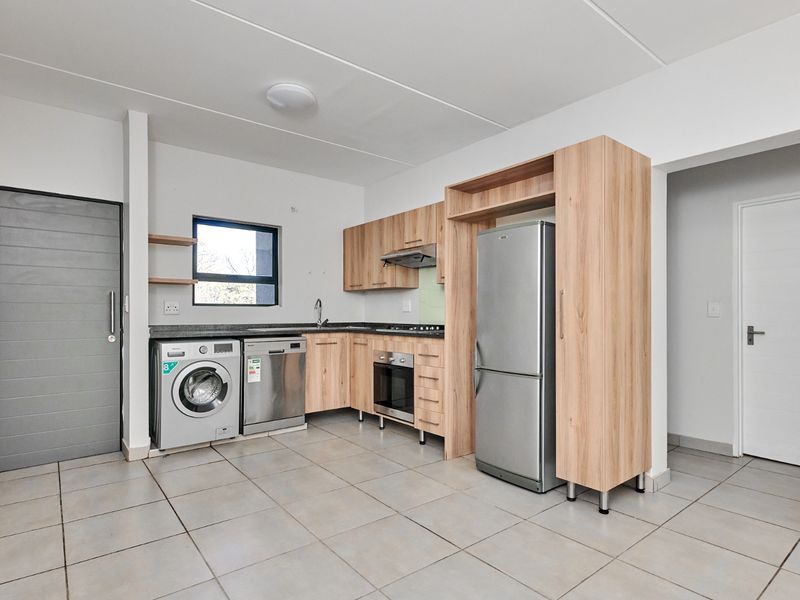 Modern kitchen featuring light wood cabinetry, integrated oven and hob, tiled flooring, and dedicated space for laundry appliances.