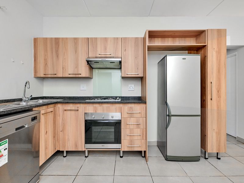 Modern kitchen featuring light wood cabinetry, granite countertops, built-in oven, gas hob, extractor fan, and tiled flooring.