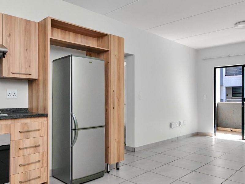 Modern open-plan kitchen and living area featuring light wood cabinetry, tiled flooring, and direct access to a private balcony.
