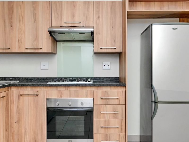 Modern kitchen featuring light wood-finish cabinetry, granite countertops, integrated gas hob, electric oven, and a dedicated space for a refrigerator.