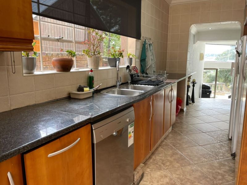 A functional kitchen featuring wooden cabinetry, granite countertops, a double sink, and tiled finishes, leading through to an adjacent living area.