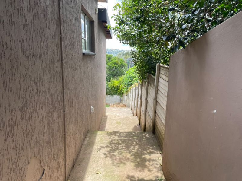 A narrow exterior side passage featuring a concrete walkway bordered by a precast boundary wall and the side elevation of the house.