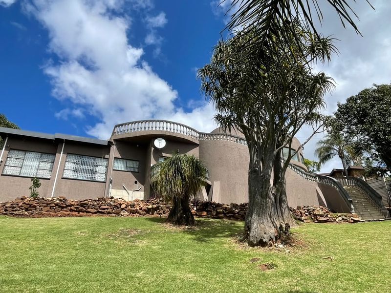 Rear view of the property featuring a curved terrace with balustrade, external staircase, and landscaped garden area.