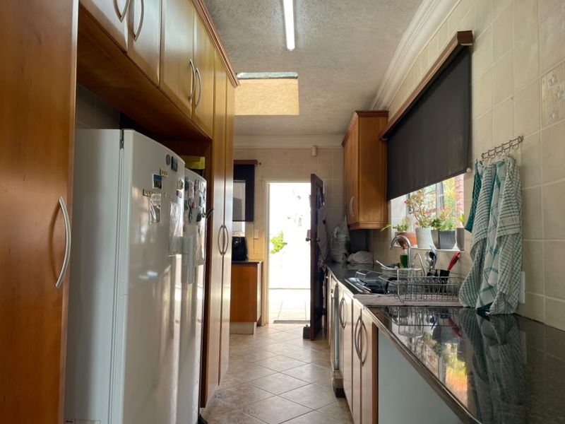 A functional galley-style kitchen featuring wood-finish cabinetry, granite countertops, tiled backsplash, and a skylight providing natural light.