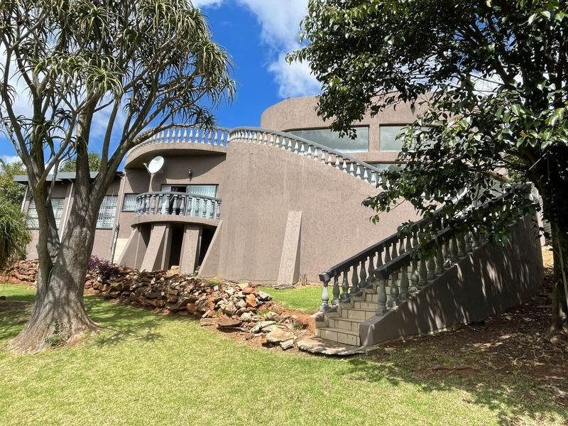 Rear view of a multi-level house featuring a curved architectural design, external staircase, balcony with balustrades, and a landscaped garden with stone retaining walls.