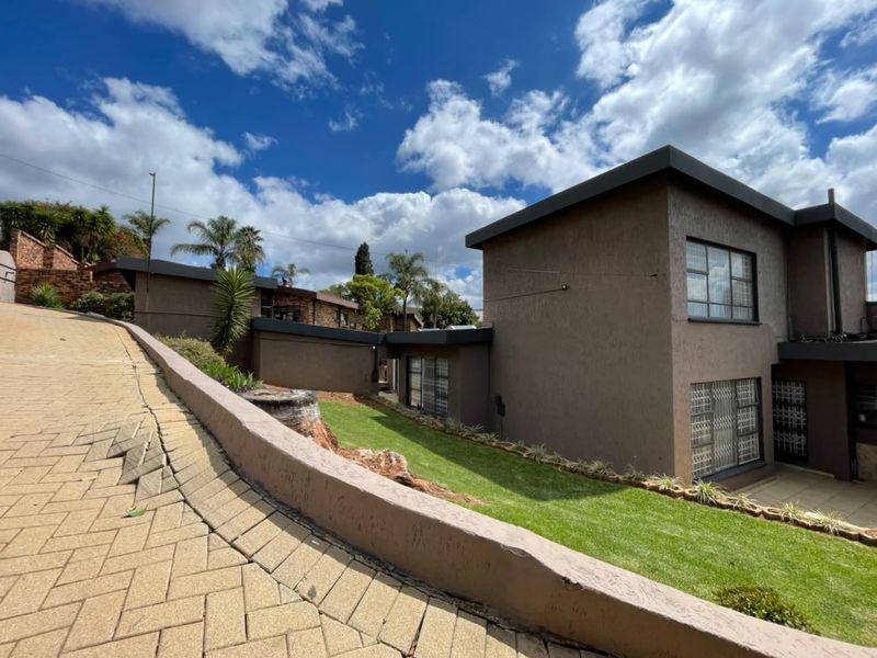 Exterior view of the property featuring a paved driveway, retaining wall, and landscaped lawn with security bars on the windows.