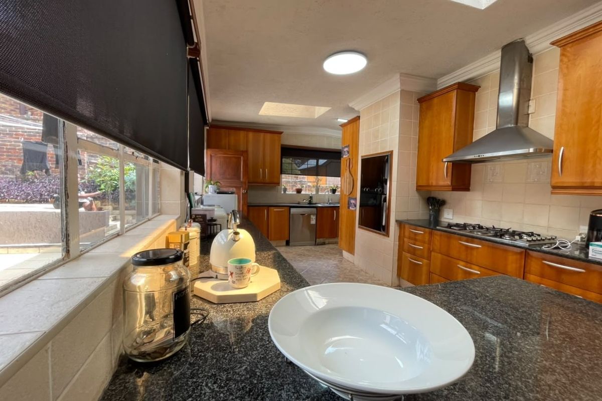 A functional kitchen featuring wooden cabinetry, granite countertops, a gas hob with extractor fan, and natural light provided by a skylight.
