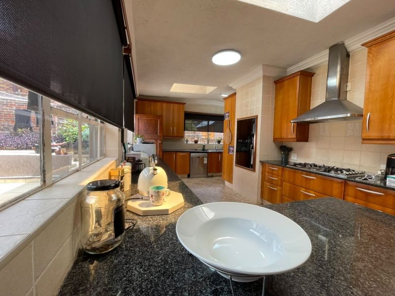 A functional kitchen featuring wooden cabinetry, granite countertops, a gas hob with extractor fan, and natural light provided by a skylight.