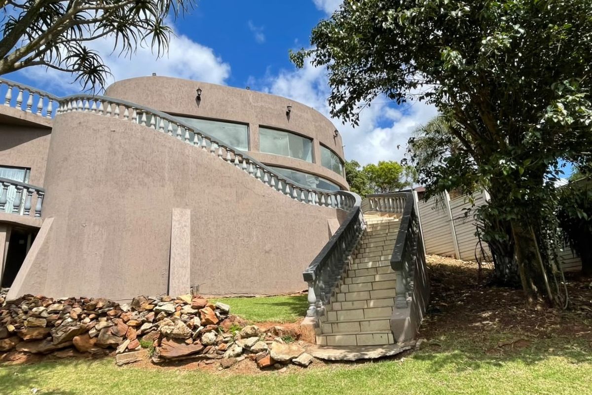 Rear view of the property featuring a distinctive curved architectural design, an external staircase with balustrades, and large windows overlooking the garden.