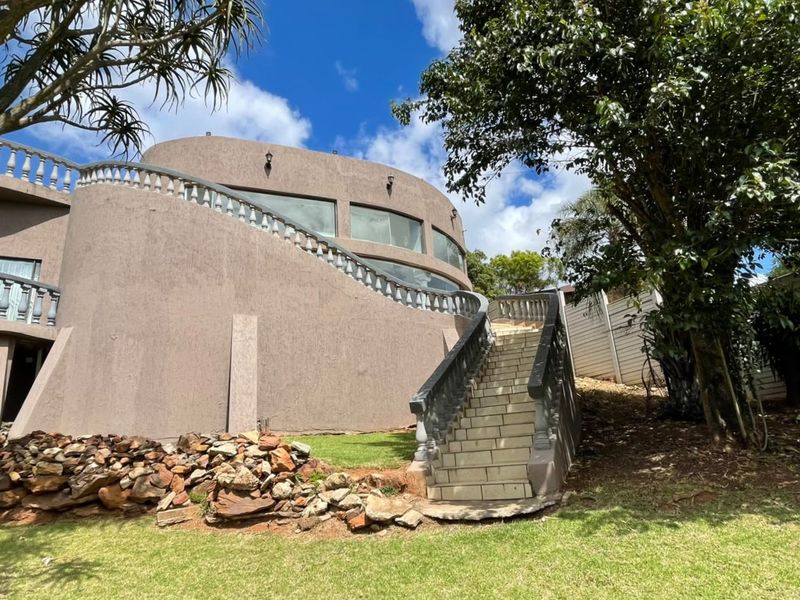 Rear view of the property featuring a distinctive curved architectural design, an external staircase with balustrades, and large windows overlooking the garden.