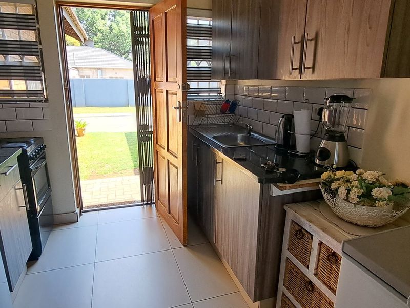 Compact kitchen featuring modern wood-finish cabinetry, subway tile backsplash, and direct access to the outdoor area through a security gate.