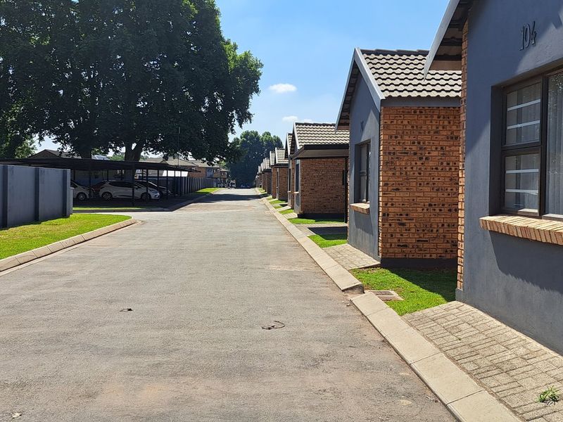 A view of the townhouse complex driveway featuring paved access, brick and rendered facades, and neat landscaping along the residential units.