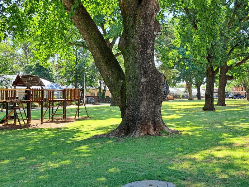 A well-maintained communal garden area featuring mature trees, expansive green lawns, and established playground equipment.