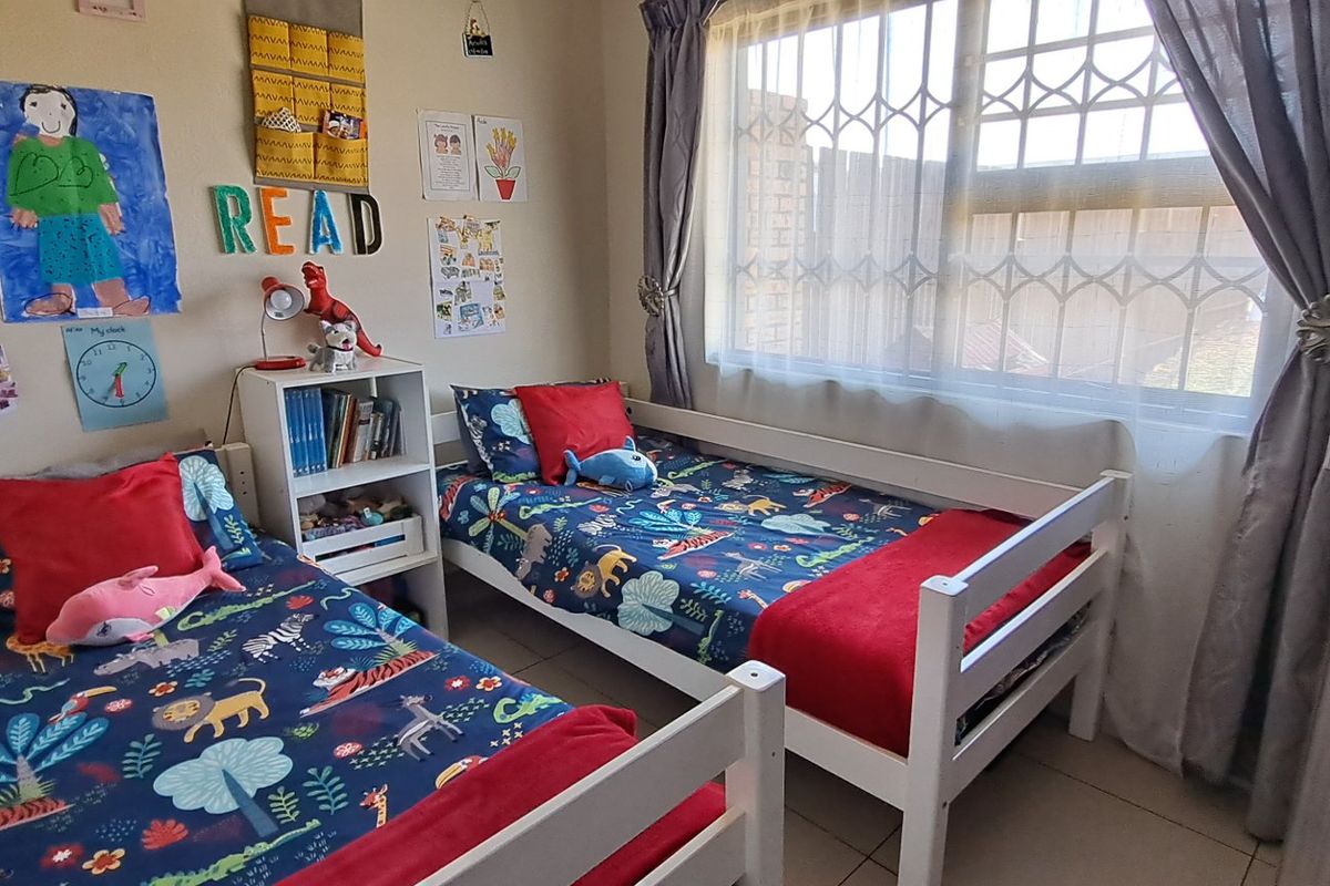 A functional bedroom featuring tiled flooring, a window with a security gate, and curtain rails, currently utilized as a children's room.
