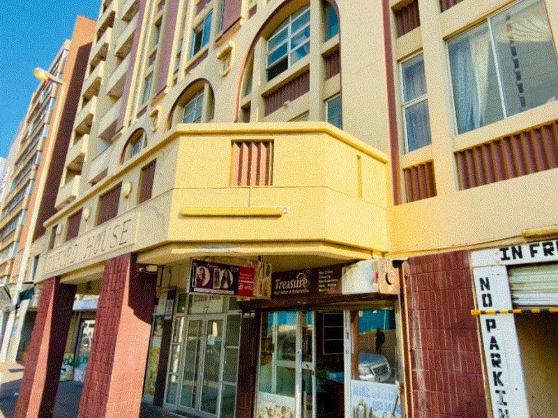 Street-level view of a multi-story apartment building featuring commercial storefronts on the ground floor and a prominent balcony structure.