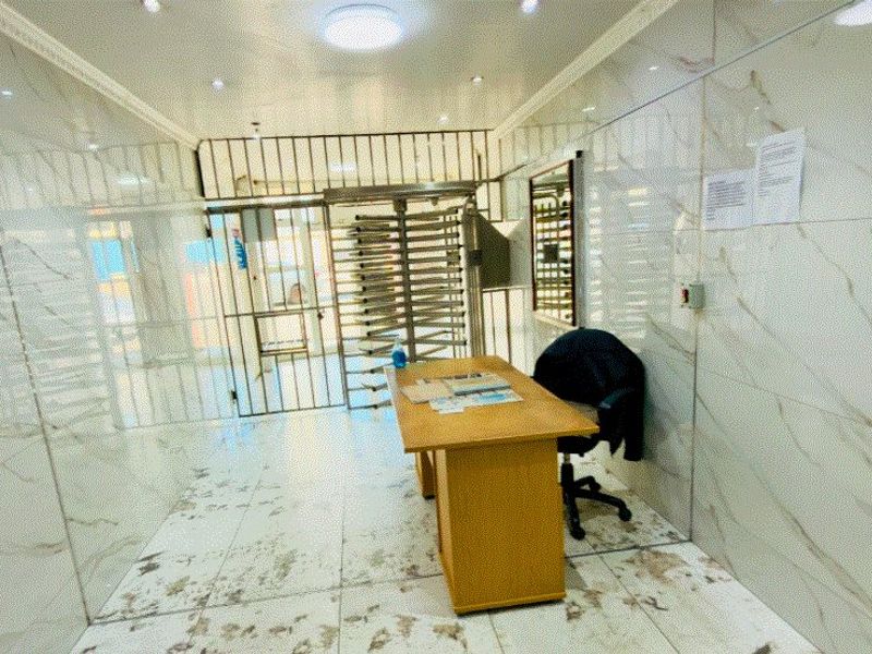 Entrance area featuring marble-look wall and floor tiling, secured by a metal turnstile and gate system.