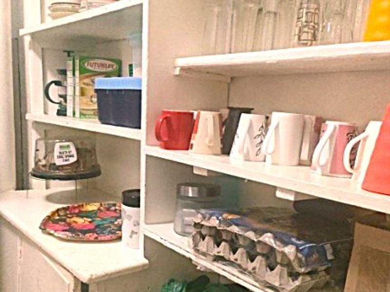 A functional pantry or scullery area featuring built-in white shelving units, providing ample storage space for kitchen essentials and dry goods.