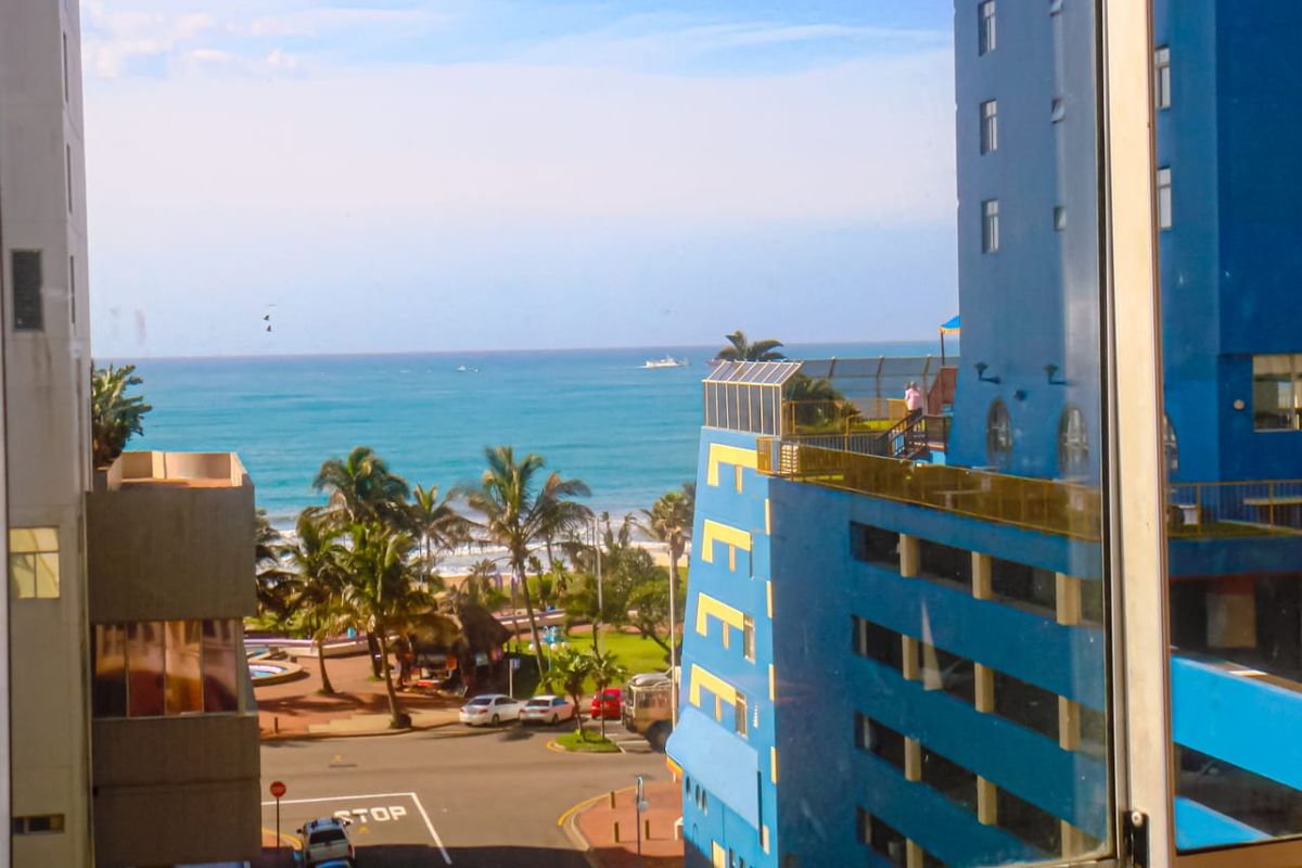 A scenic view from an apartment window overlooking the ocean, nearby buildings, and street level.