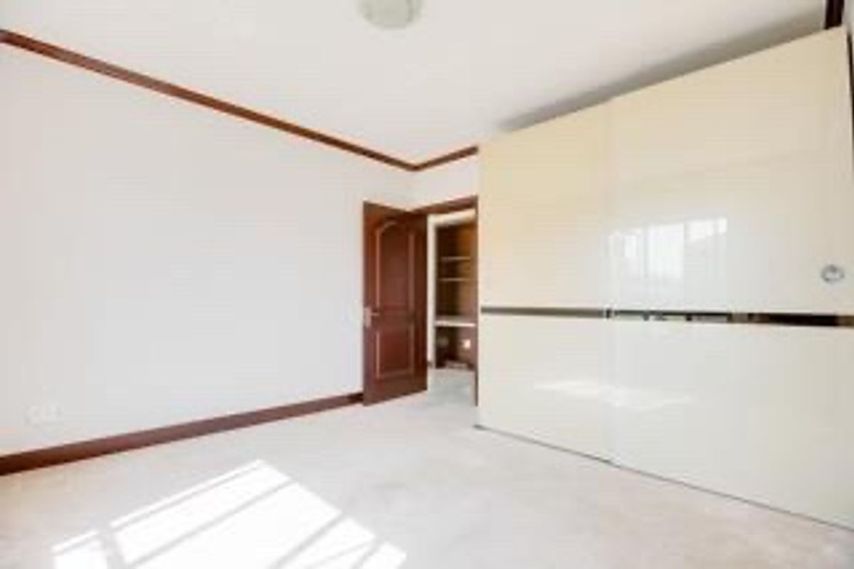 A bright, empty bedroom featuring a large built-in sliding door wardrobe, wooden door, and crown molding details.