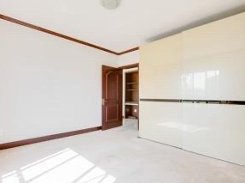 A bright, empty bedroom featuring a large built-in sliding door wardrobe, wooden door, and crown molding details.