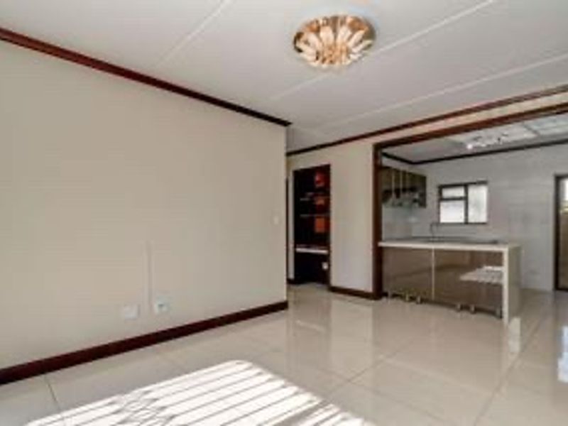 An open-plan living and kitchen area featuring tiled flooring, neutral walls, and built-in kitchen cabinetry, offering a clean and versatile space.