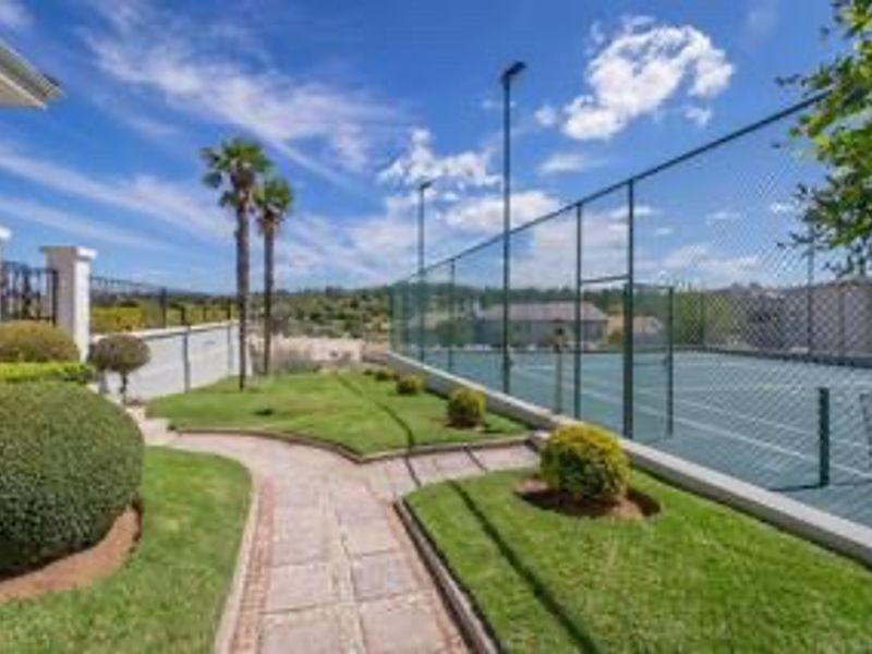 Well-maintained private tennis court featuring chain-link fencing, floodlights, and an adjacent paved garden walkway.