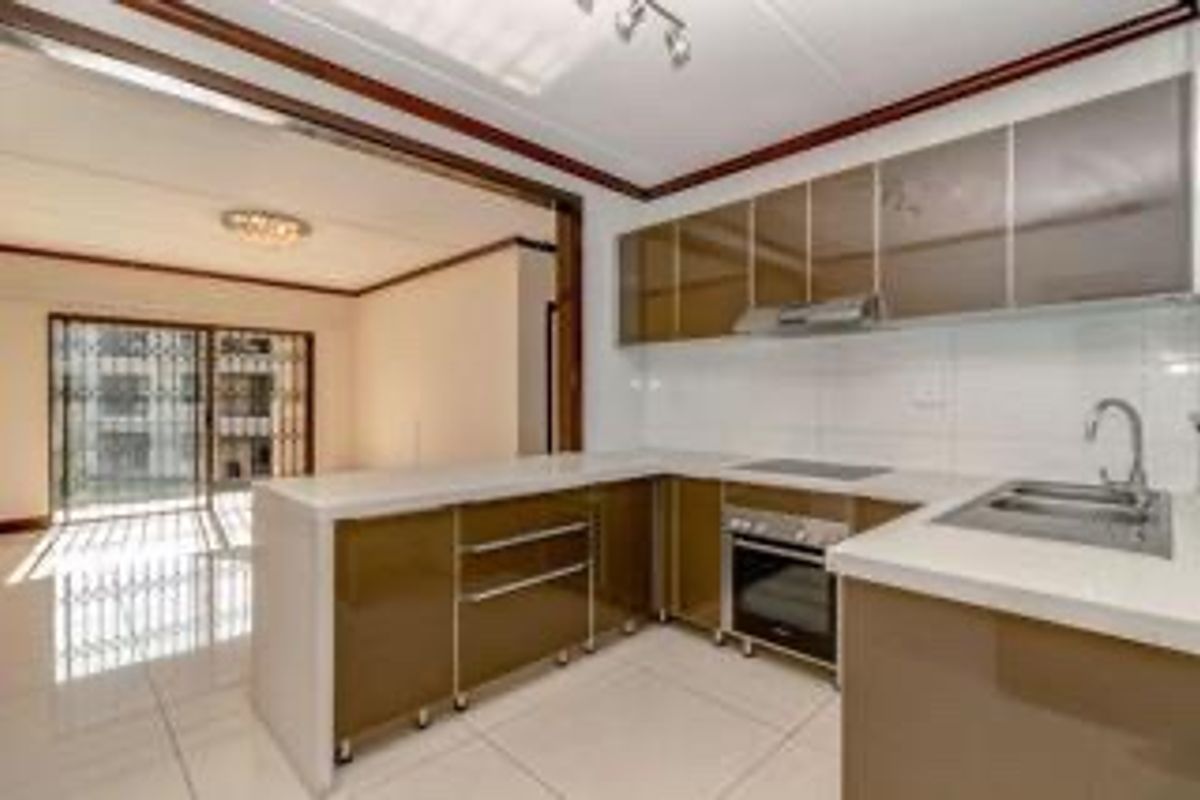 Modern open-plan kitchen featuring sleek cabinetry, integrated appliances, and tiled flooring, seamlessly flowing into a bright living area with access to a balcony.