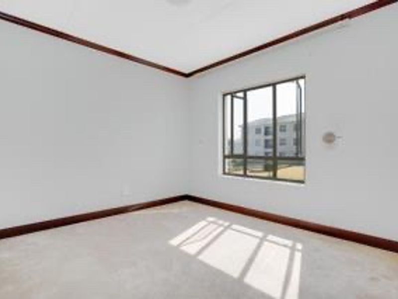 A bright, empty bedroom featuring neutral carpeting, timber crown molding, and baseboards, with a large window providing natural light.