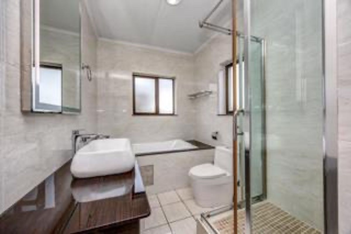 A modern, well-maintained bathroom featuring a vessel sink, built-in bathtub, glass-enclosed shower, and neutral tiled finishes throughout.