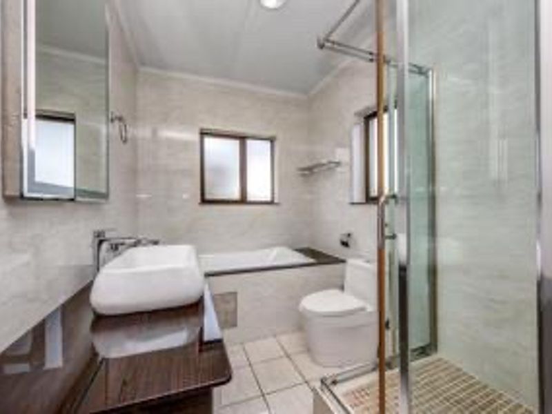 A modern, well-maintained bathroom featuring a vessel sink, built-in bathtub, glass-enclosed shower, and neutral tiled finishes throughout.